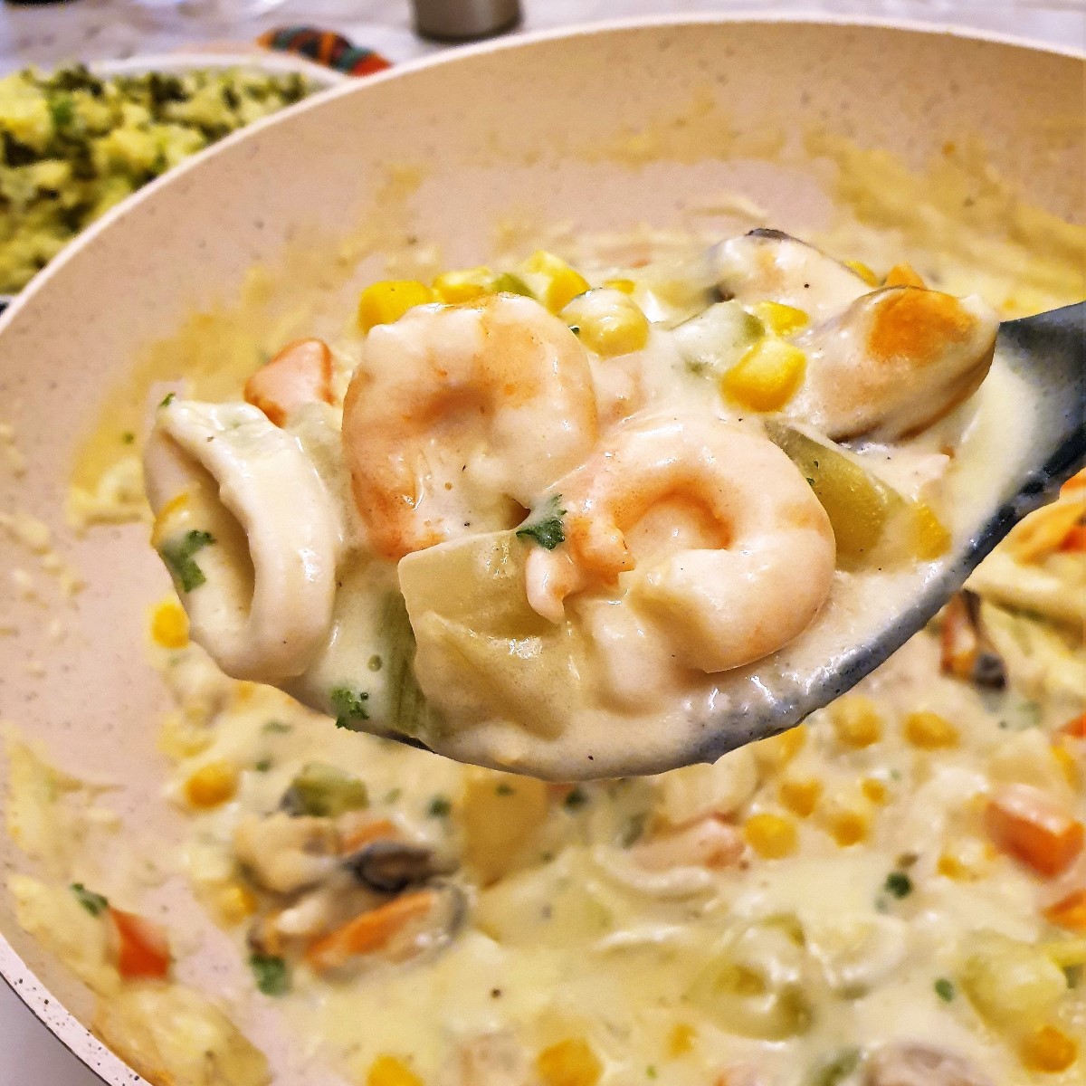 Prawns and mussels in a creamy sauce on a serving spoon.