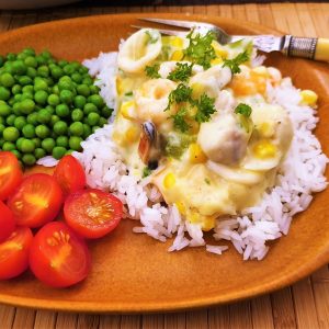 Close up of seafood a la king on a plate with peas and tomatoes.