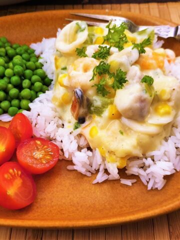 Close up of seafood a la king on a plate with peas and tomatoes.