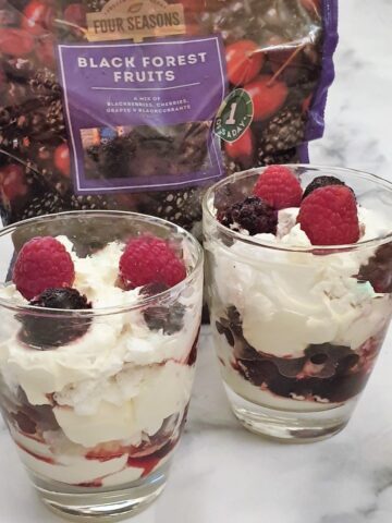 Two glasses of eton mess in front of a bag of frozen berries.