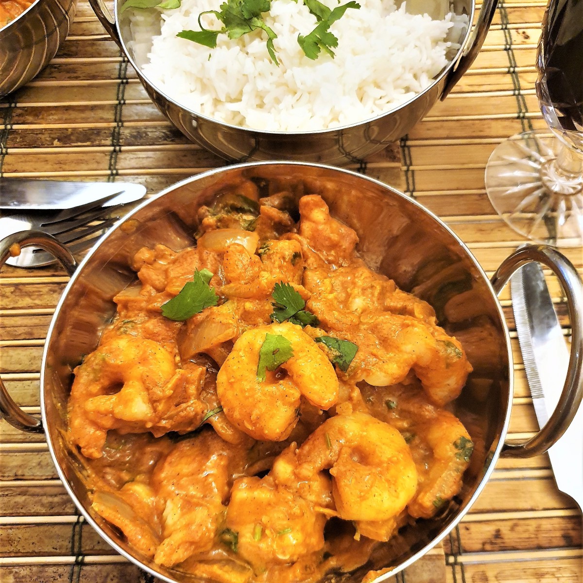 Kashmiri chicken and prawn curry in a dish in front of a bowl of white rice.