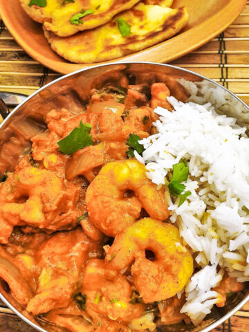 Kashmiri chicken and prawn curry in a dish in front of a plate of homemade buttered naan bread.