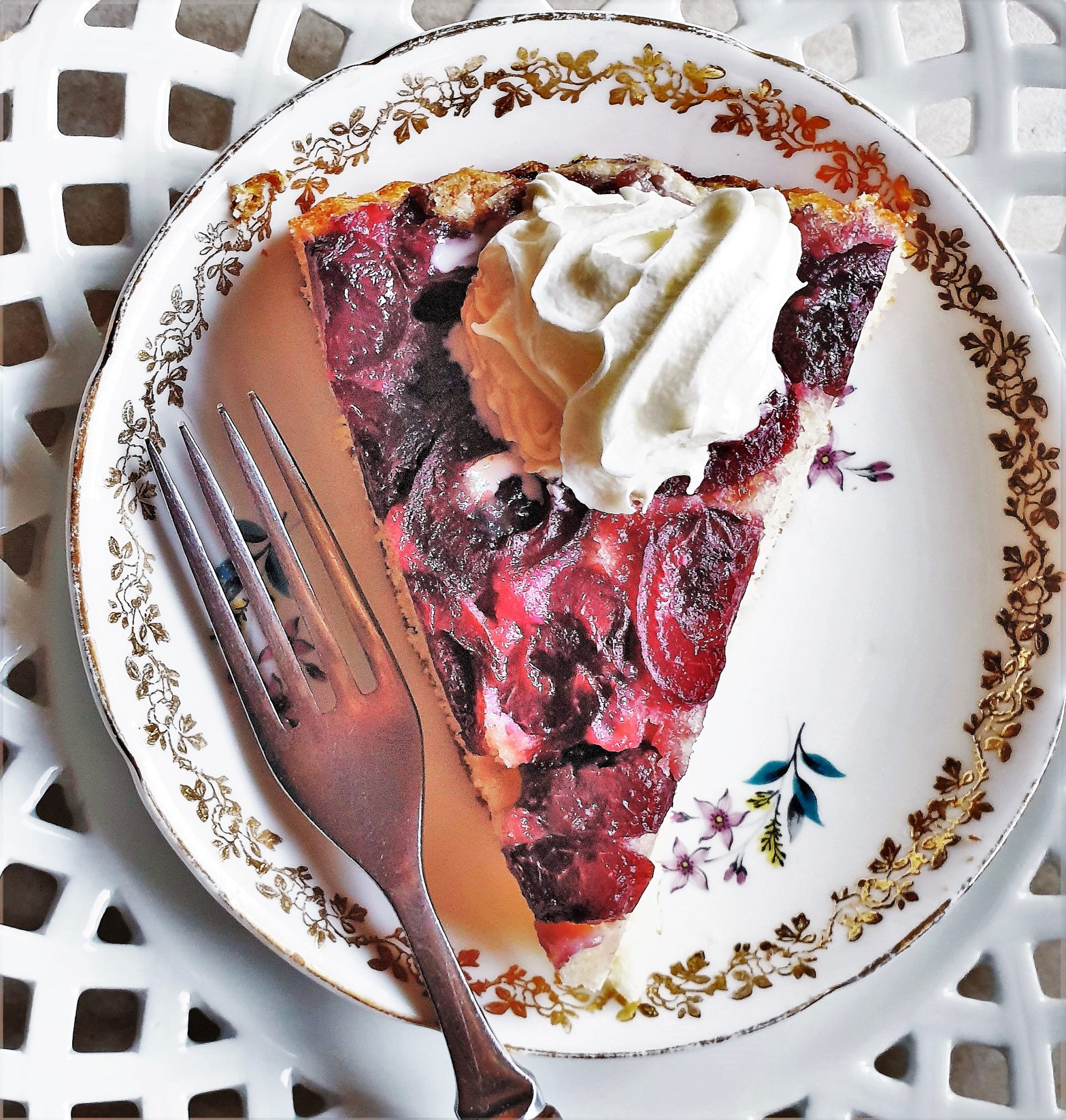 A slice of cherry cake on a plate, topped with whipped cream.