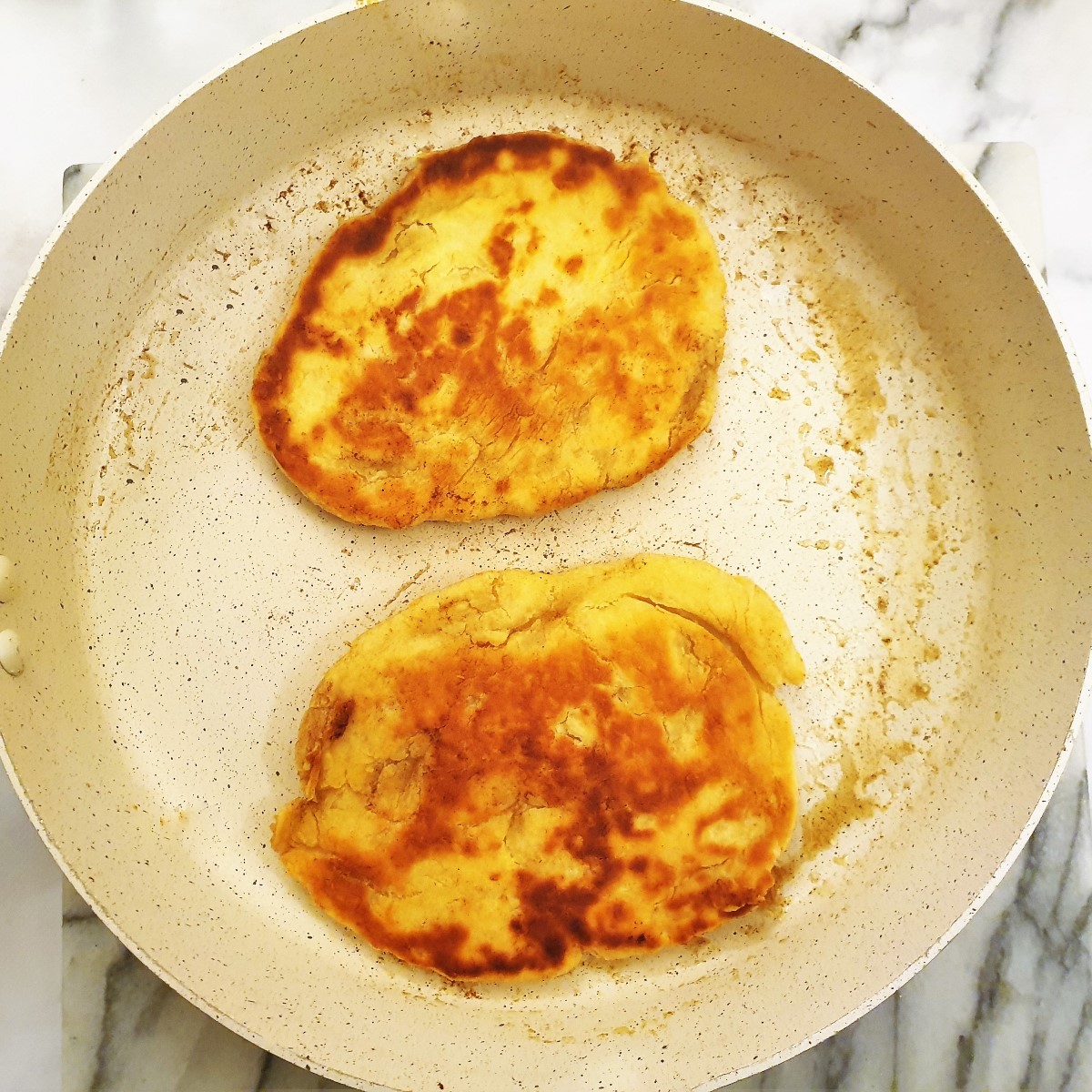 2 pieces of naan bread browning in butter in a frying pan.