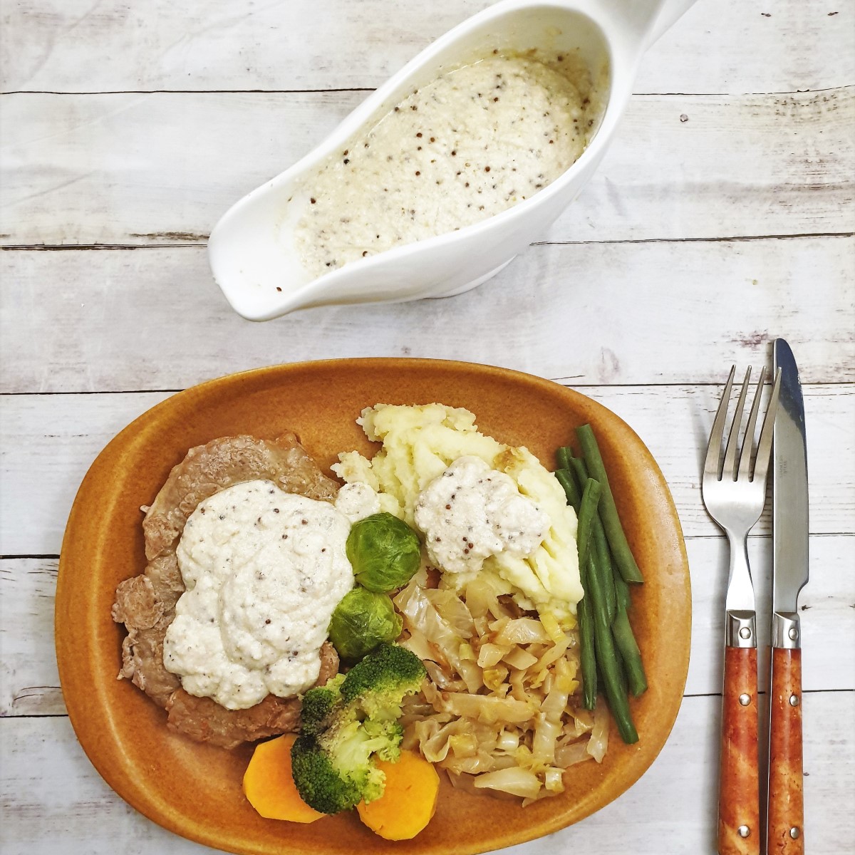 Overhead shop of honey mustard gravy in a gravy boat, along side a plate of food.