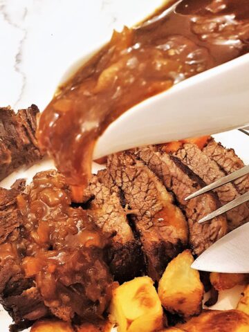 Onion gravy being poured over a plate of succulent slow-roasted brisket.