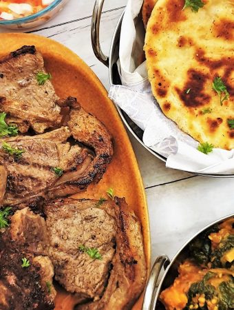 Tandori lamb chops on a plate with naan bread and saag aloo.