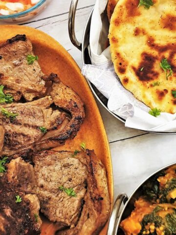 Tandori lamb chops on a plate with naan bread and saag aloo.