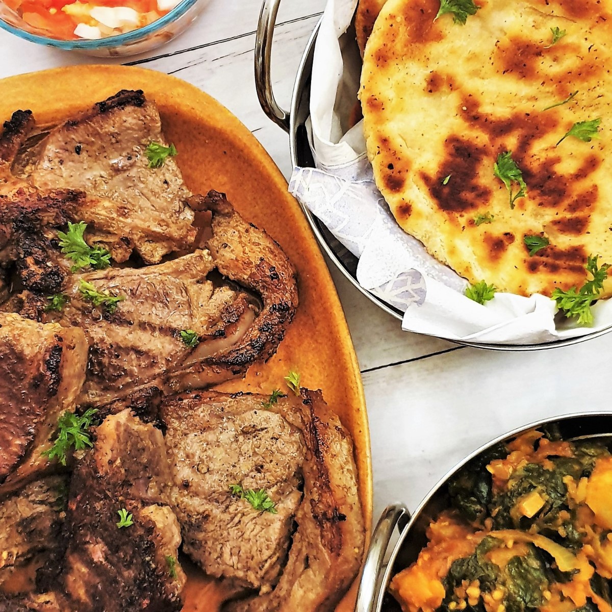 Tandoori lamb chops on a plate with naan bread and saag aloo.