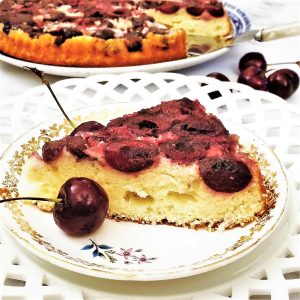 A slice of upside down cherry cake next to fresh cherries.