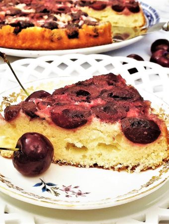 A slice of upside down cherry cake next to fresh cherries.