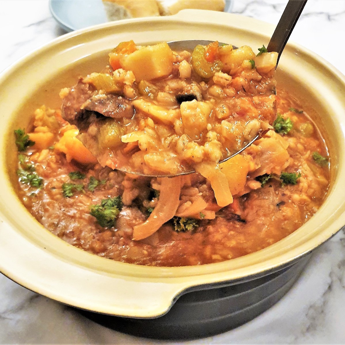 Close up of a ladleful of beef and barley stew being lifted from the serving dish.