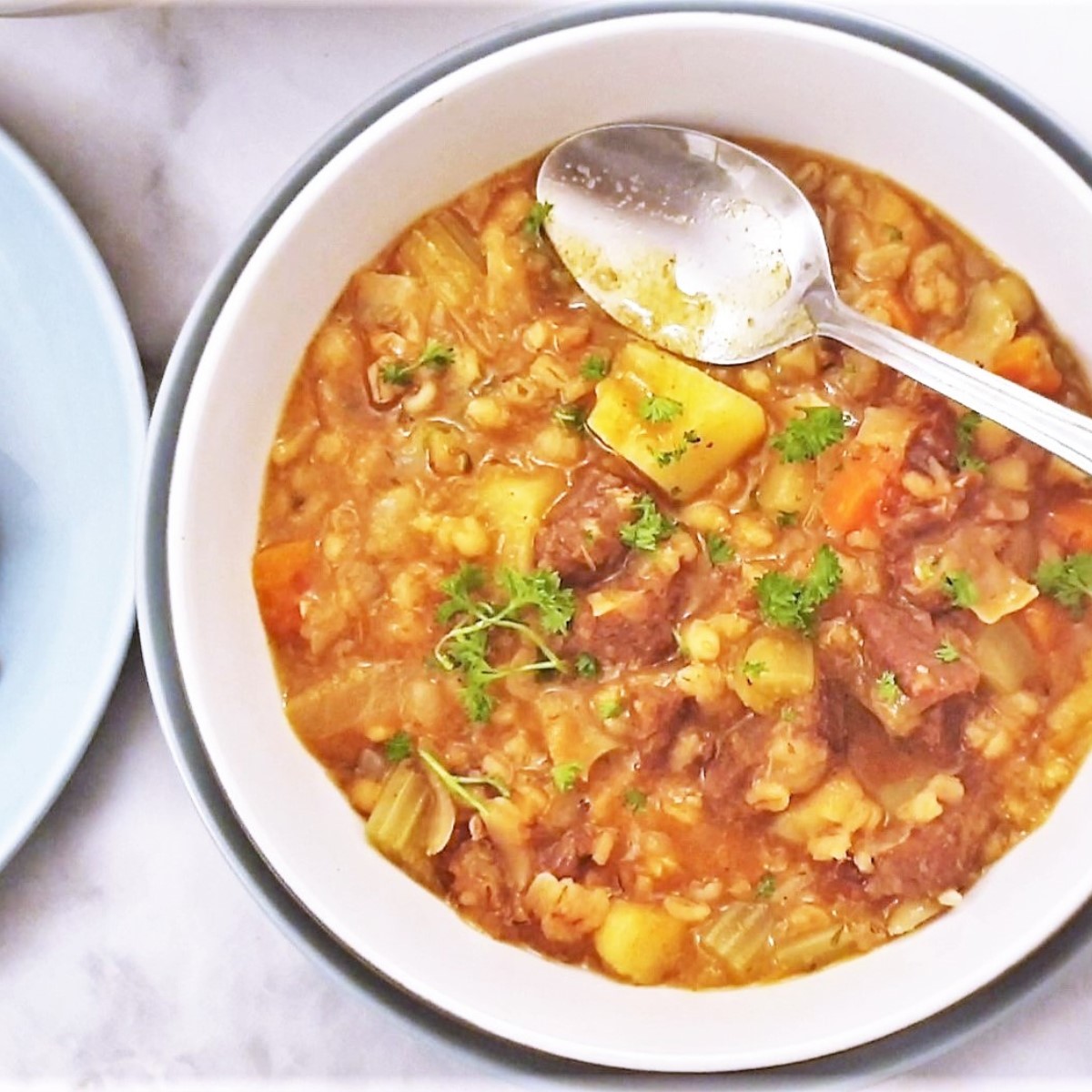 A bowl of beef and barley stew with a spoon.