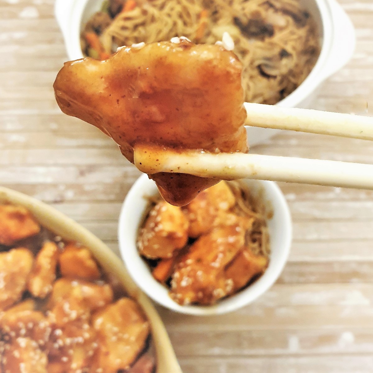 A piece of chicken coated with sesae sauce held in a pair of chopsticks.