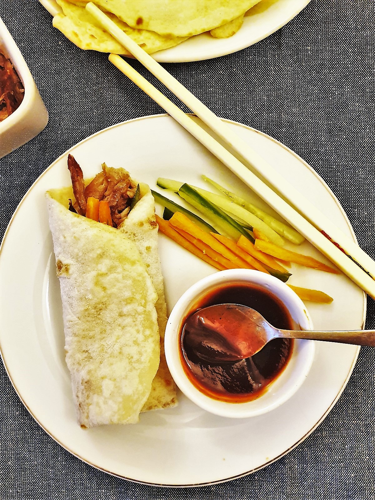 A rolled duck pancake on a plate with a dish of hoisin sauce.