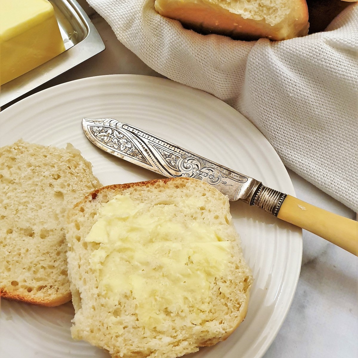 A dinner roll spread with butter on a plate with a knife.