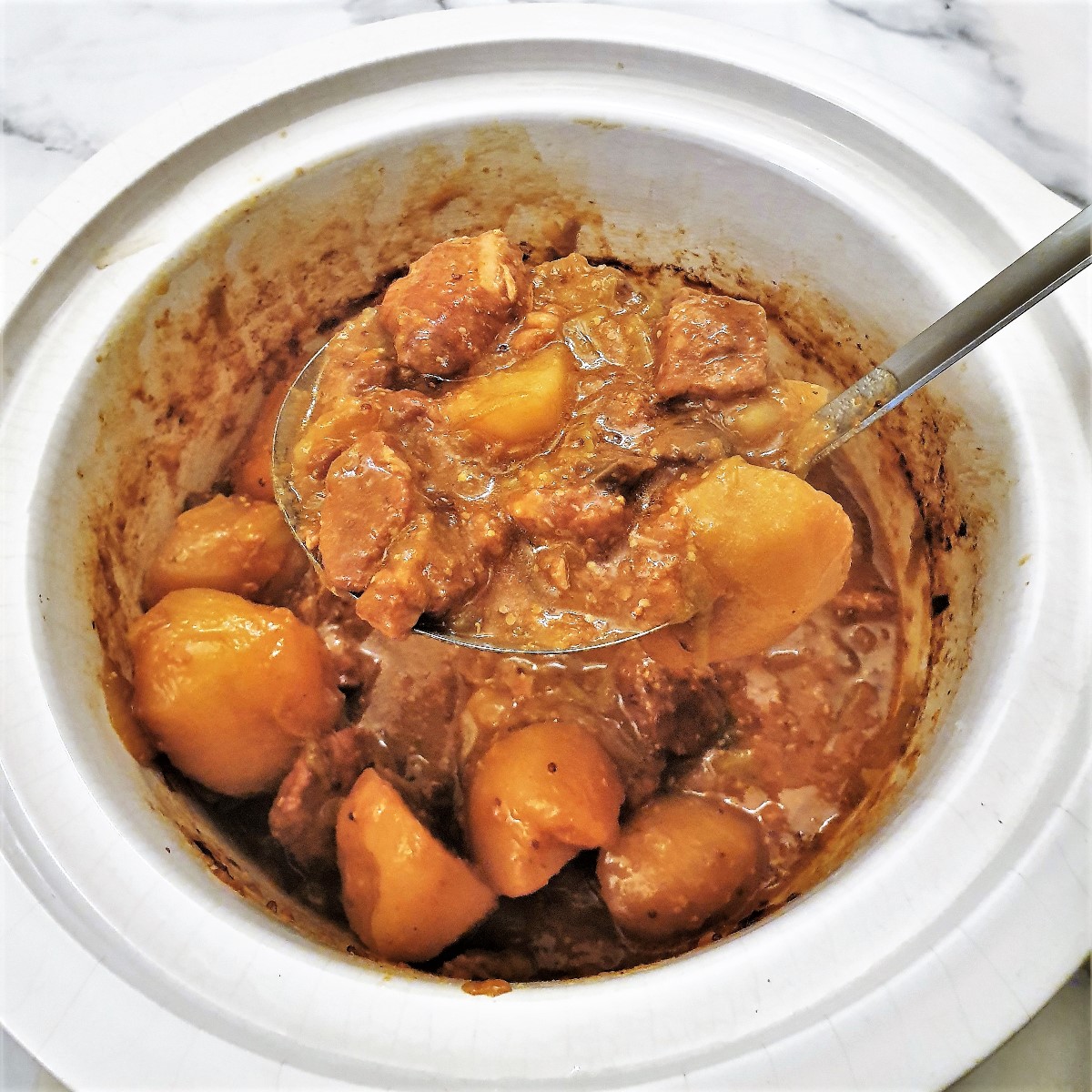 A ladle of honey mushroom pork casserole being lifted from th slow cooker.