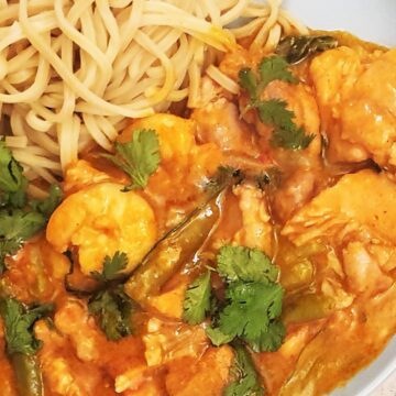 Closeup of a plate of thai red curry with chicken and prawns.