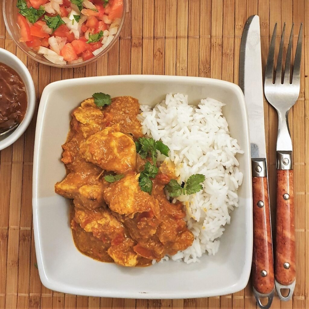 Overhead shot of a bowl of chicken tikka masala with tomato sambal and chutney.