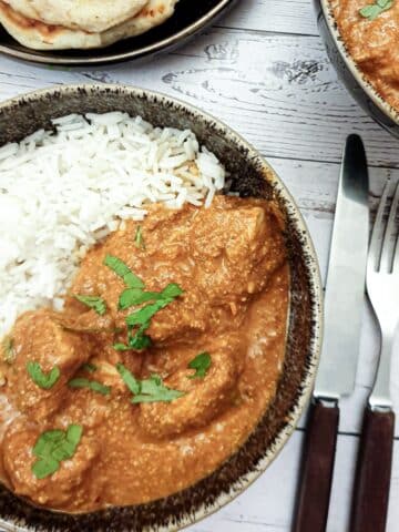 Chicken tikka masla in a bowl with rice next to a plate of naan bread.