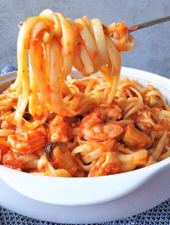 Pasta wrapped around a fork held over a bowl of pasta pescatore.
