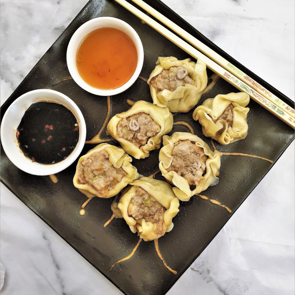 Overhead shot of a plate of steamed pork and shrimp dumplings with 2 dipping sauces.