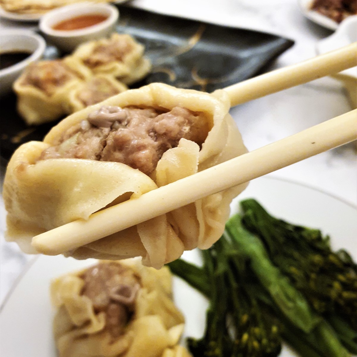 A pork and shrimp dumpling held in chopsticks.