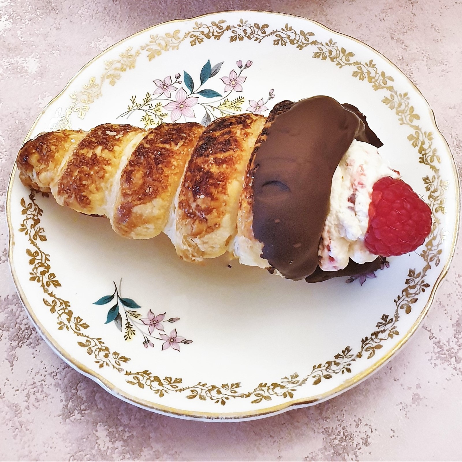 A chocolate-coated raspberry cream horn on a plate.