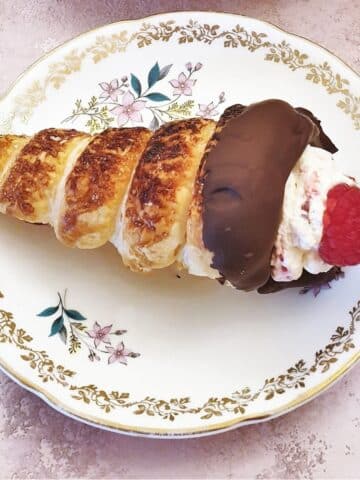 A chocolate-coated raspberry cream horn on a plate.