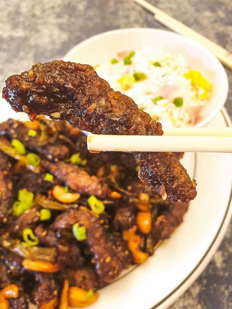 A single slice of dragon beef held above the bowl.