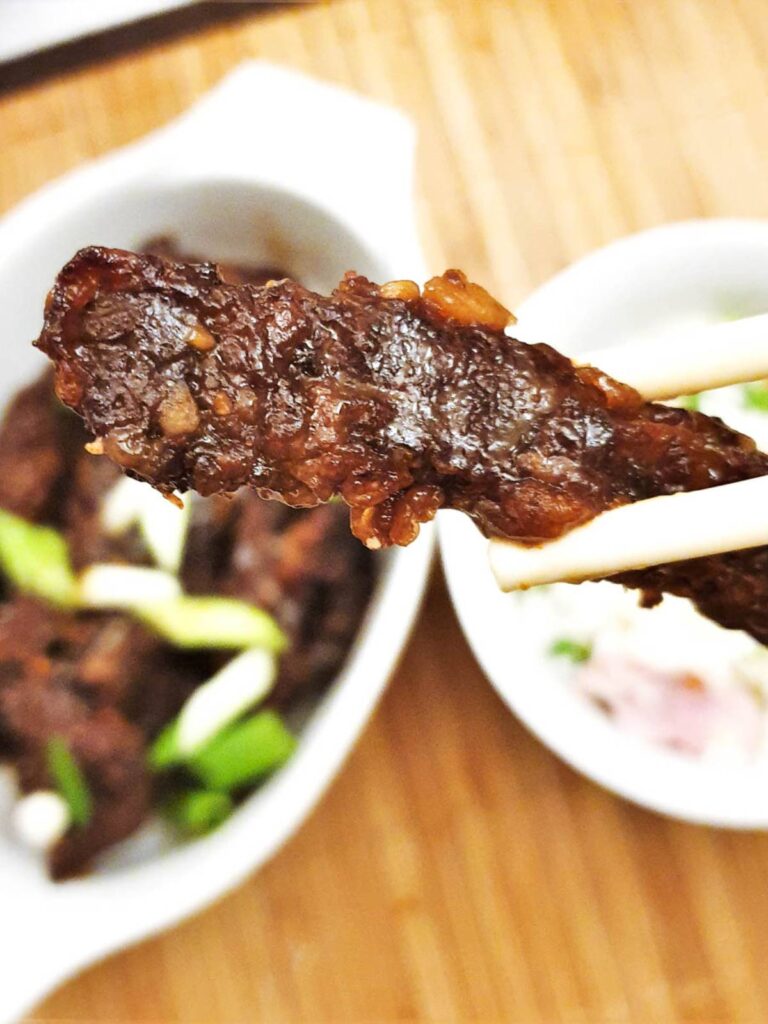 A slice of dragon beef held in chopsticks.