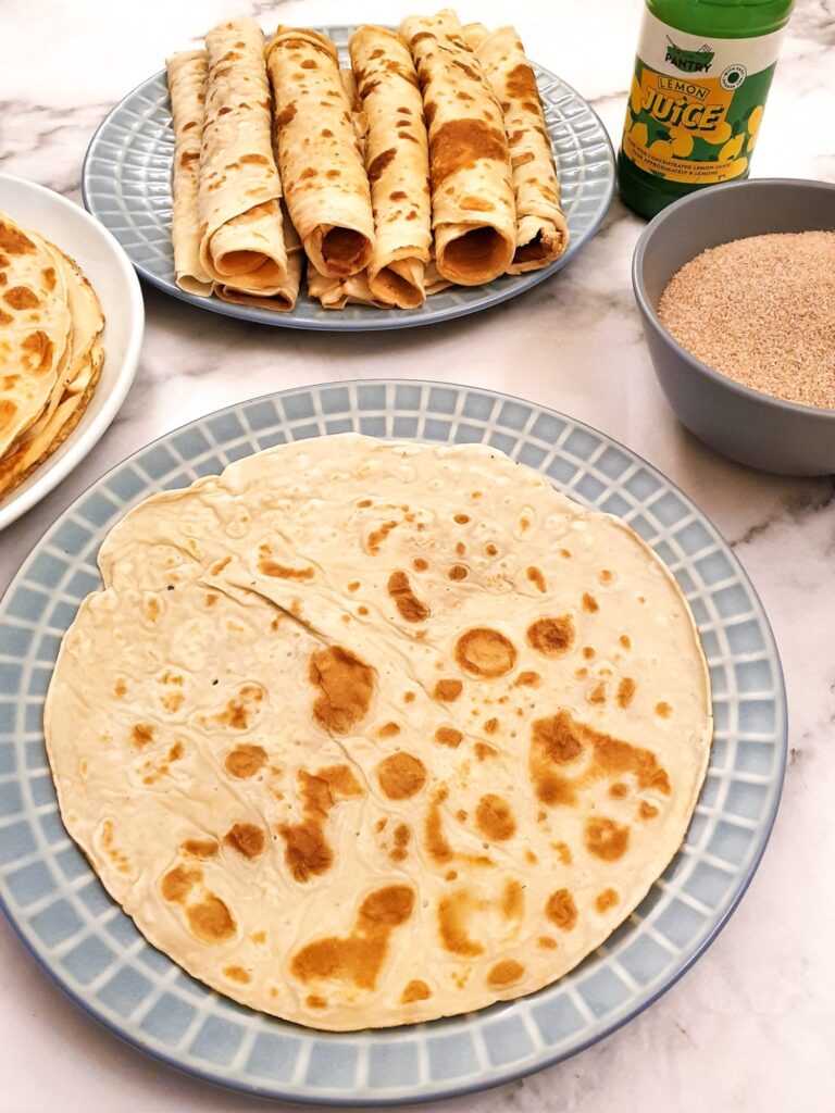 A pancake on a plate next to a dish of cinnamon sugar.