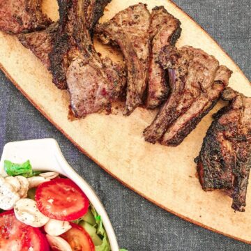 Barbequed minted lamb chops on a platter next to a dish of green salad.