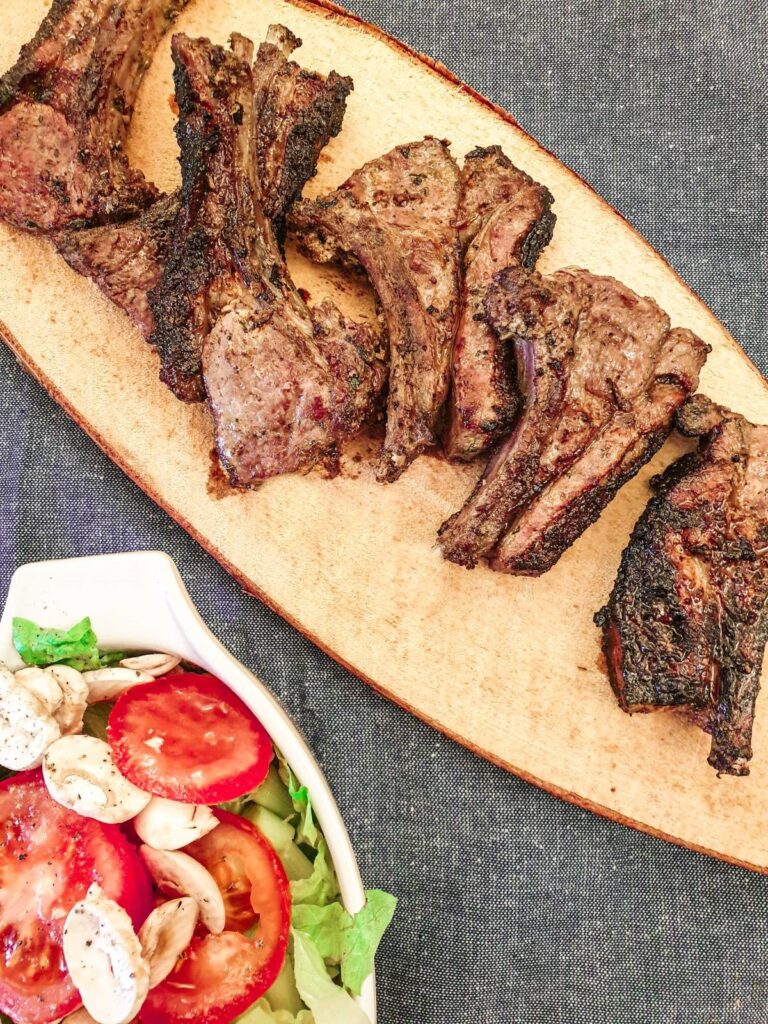 Barbequed minted lamb chops on a platter next to a dish of green salad.