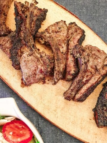 Barbequed minted lamb chops on a platter next to a dish of green salad.