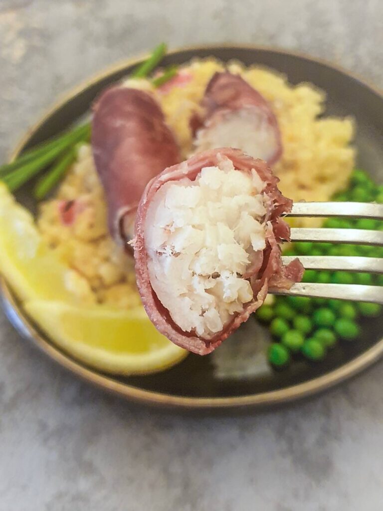 A piece of serrno ham wrapped monkfish on a fork.