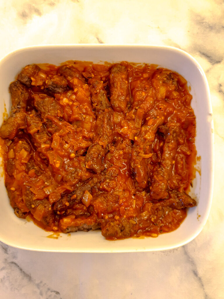 A serving dish of beef strips covered with marinara sauce.