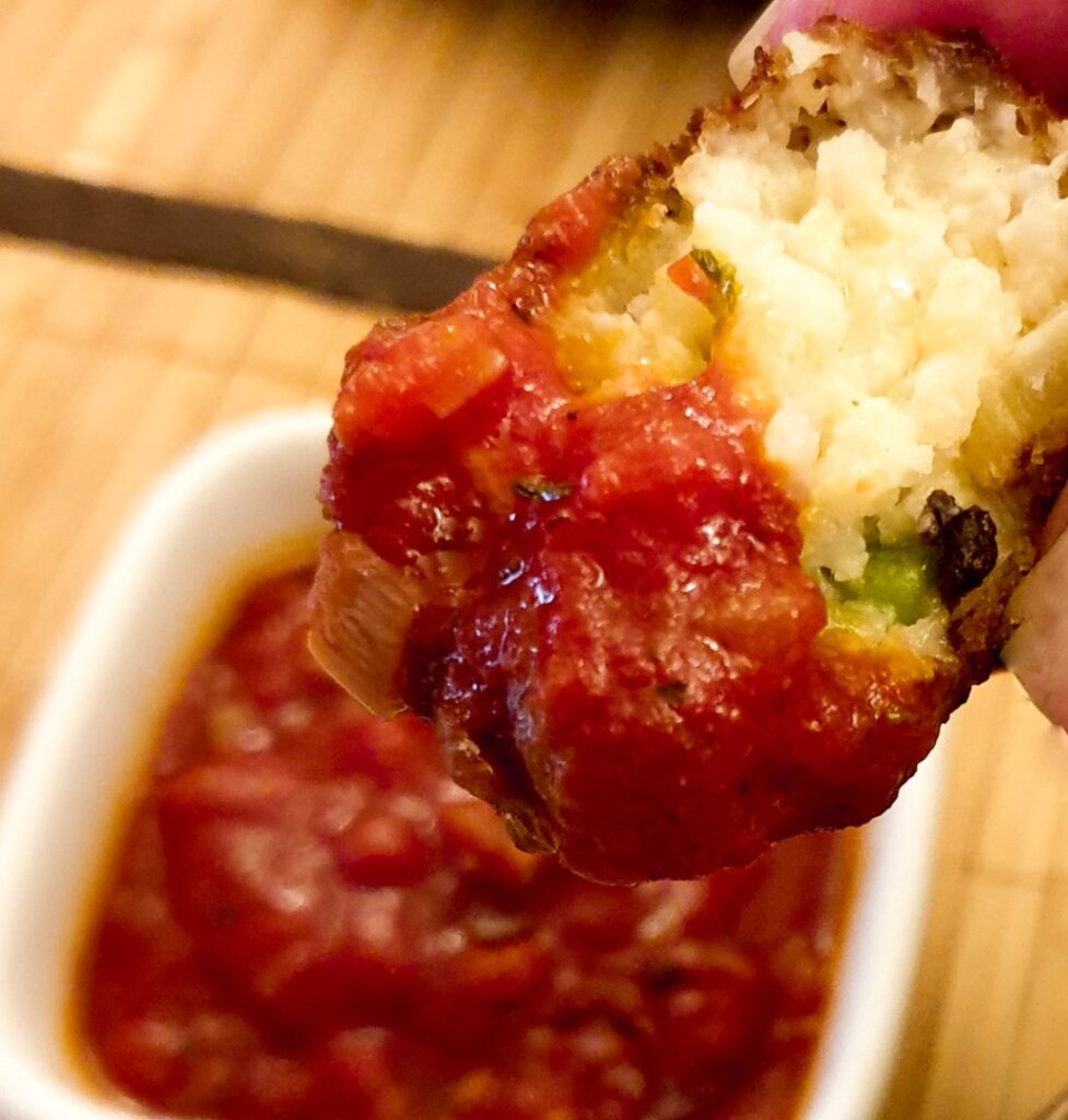 Half an arancino dipped in tomato sauce.