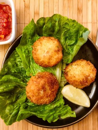 Three arancini on plate next to a dish of tangy homemade tomato sauce.