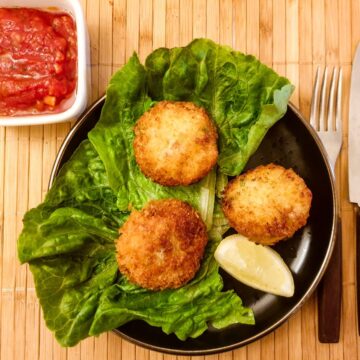 Three arancini on plate next to a dish of tangy homemade tomato sauce.