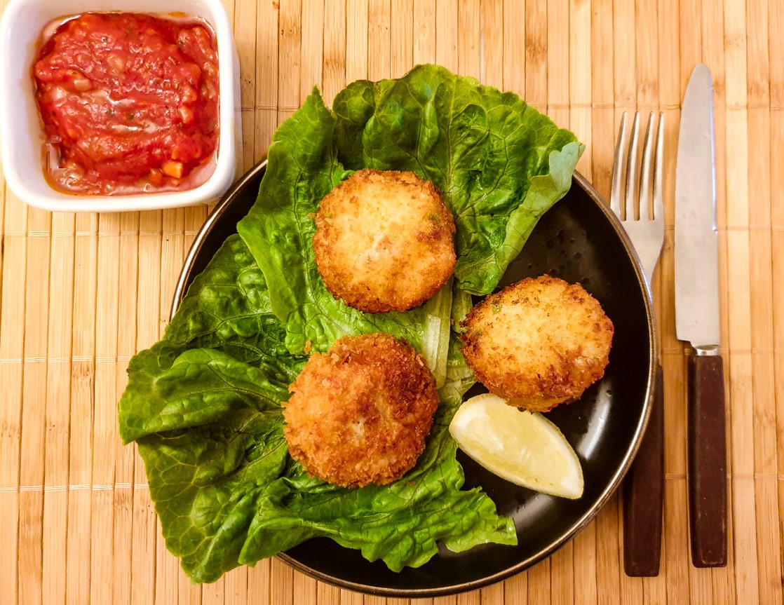 Three arancini on plate next to a dish of tangy homemade tomato sauce.