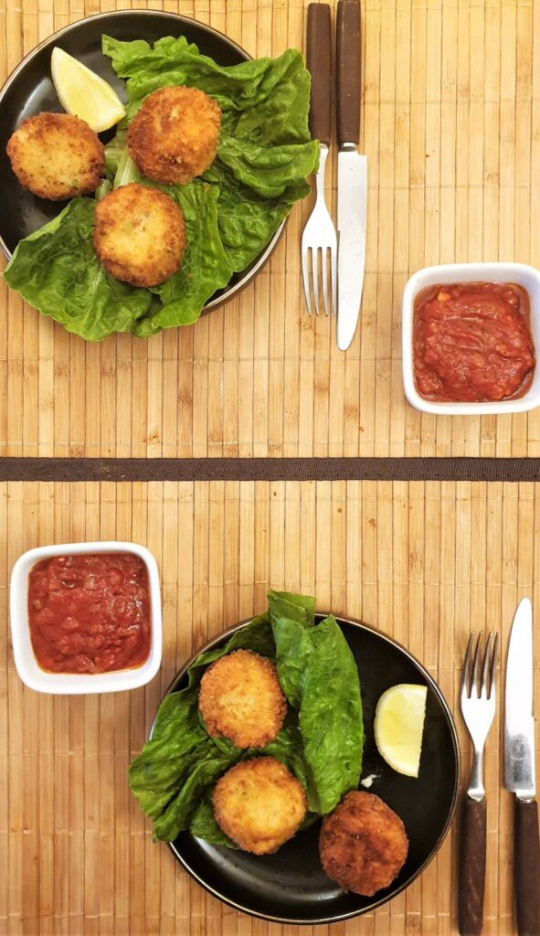 Overhead shot of two plates of arancini balls with bowls of homemade tomato sauce.