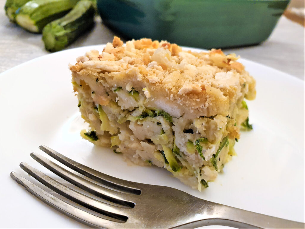 A slice of cheesy zucchini bake on a plate with a fork.