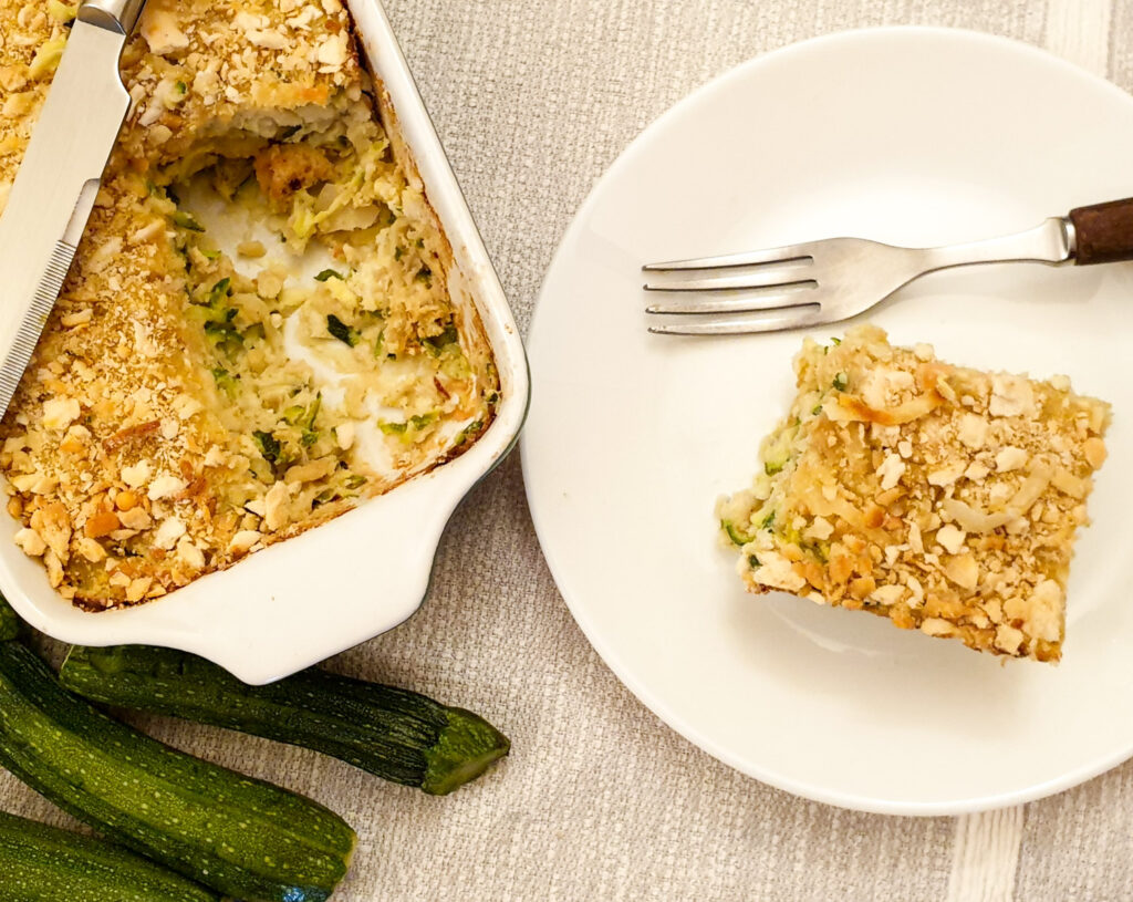 Overhead view of a slice of zucchini bake on a plate next to serving dish.