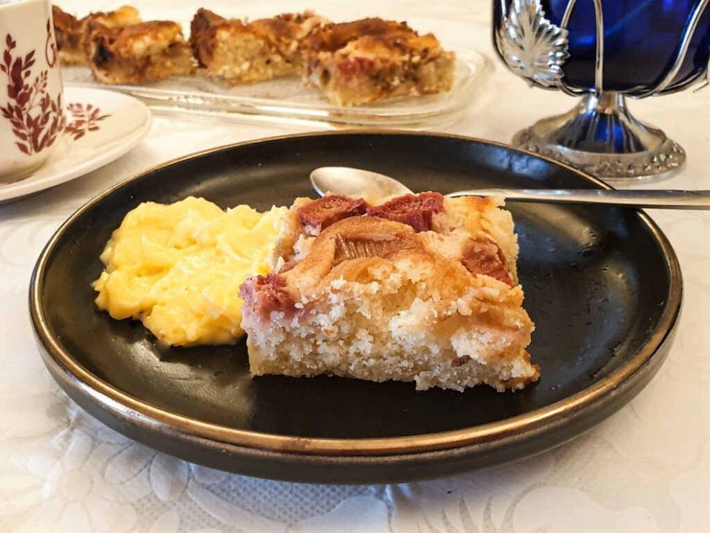 A slice of rhubarb cake on a plate, with custard.