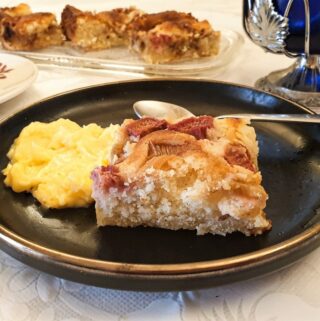 A slice of creamy rhubarb cake on a plate, with custard.