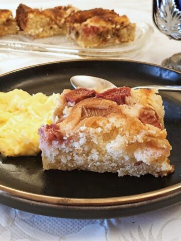 A slice of creamy rhubarb cake on a plate, with custard.