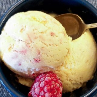A scoop of homemade raspberry ripple ice cream in a dish with a raspberry.