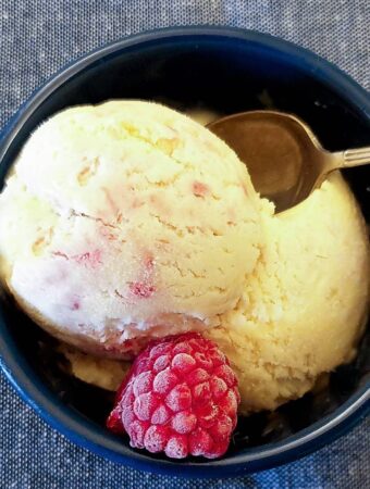 A scoop of homemade raspberry ripple ice cream in a dish with a raspberry.