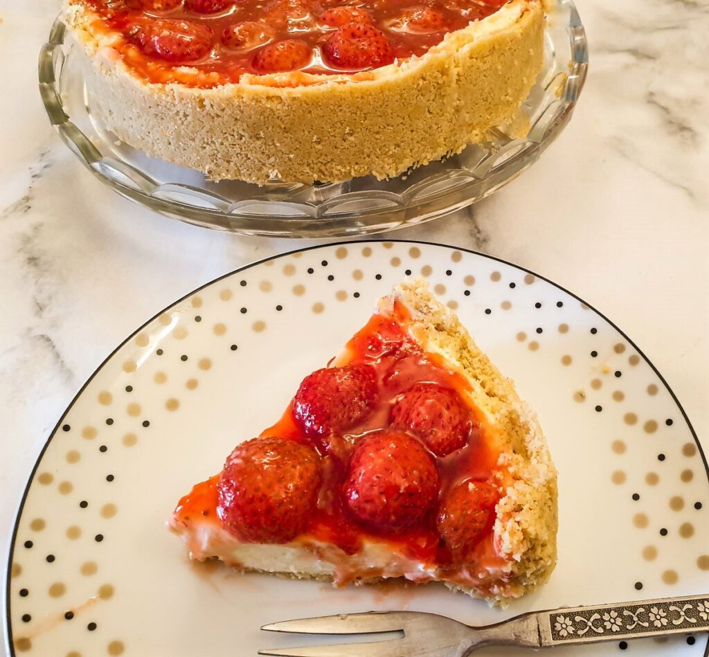 Strawberry cheesecake on a plate next to the whole cheesecake.
